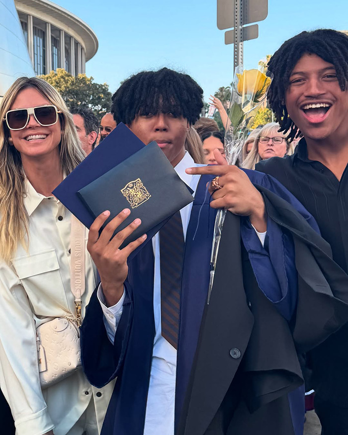 Heidi Klum with two young men celebrating graduation outdoors on a sunny day, smiling and holding diplomas.