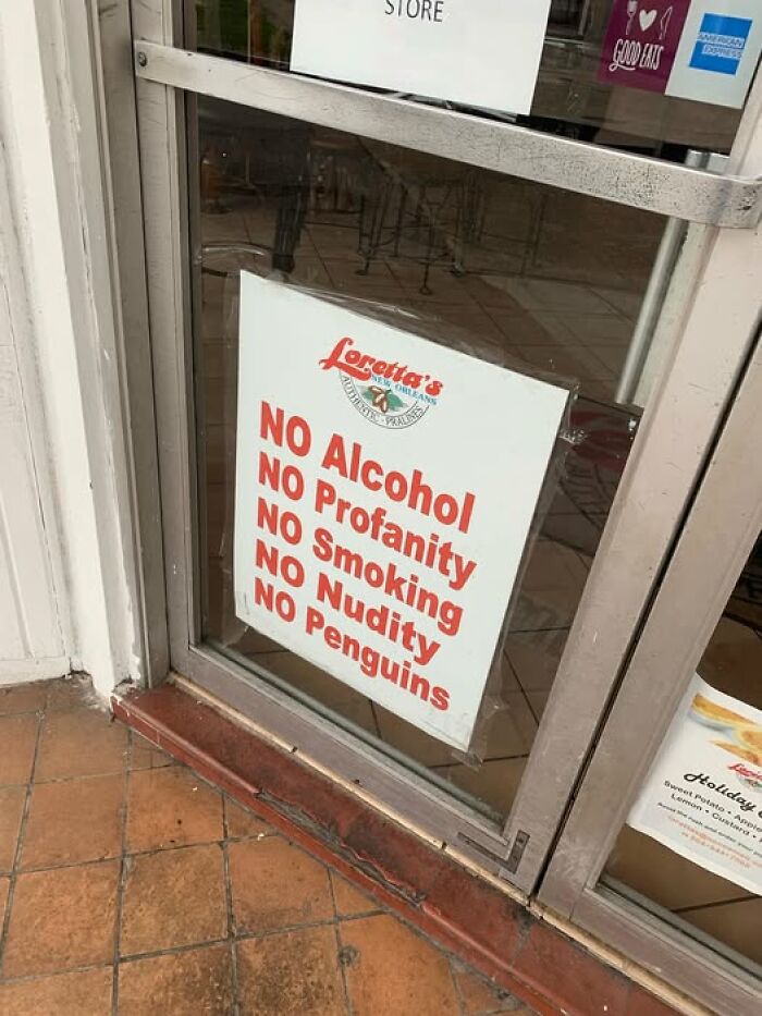 Funny sign on restaurant door listing unusual rules including no alcohol, profanity, smoking, nudity, or penguins visible through glass.