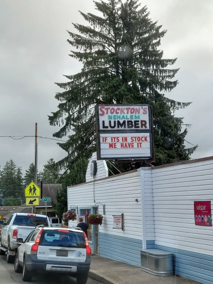 Humorous lumber store sign with a funny message adds chaos and laughter to the world on a cloudy day.