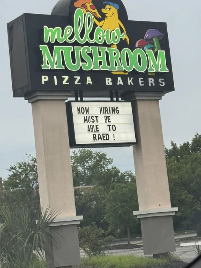 Mellow Mushroom pizza sign with a humorous hiring message containing a spelling error, adding chaos to the world.