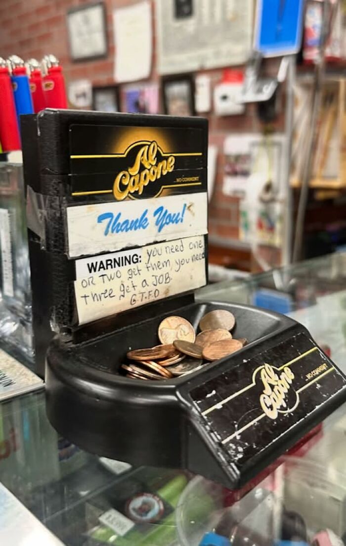 Al Capone cigar ashtray with a handwritten warning sign adding chaos humor at a store counter with loose change.