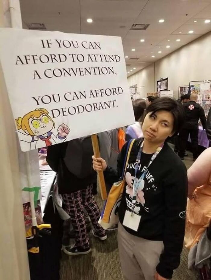 Person at a convention holding a hilarious sign about deodorant amid chaotic and funny event moments.