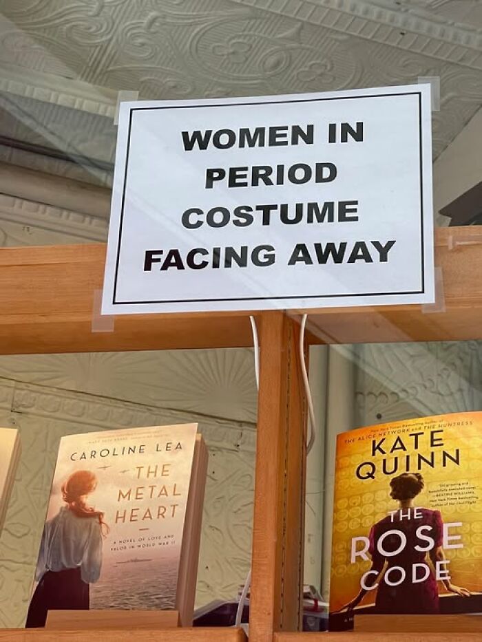 Sign humorously directing women in period costume facing away, adding chaos to the world in a bookstore setting.