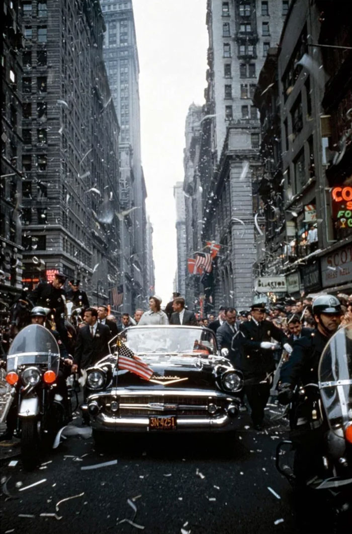 Vintage car parade with police escort moving through a crowded city street in a fascinating historical photo.