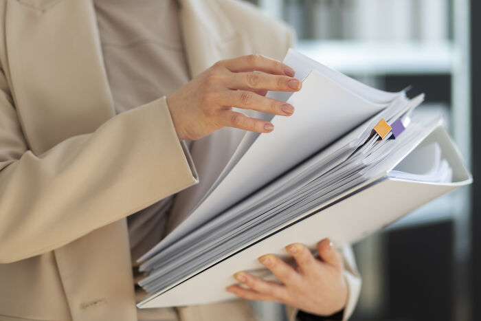 Person in beige suit holding and flipping through a thick binder of documents about folks from history.