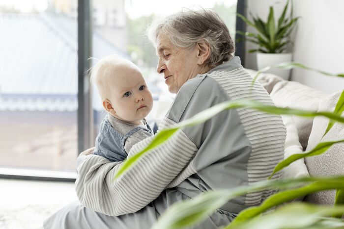Elderly woman holding baby indoors, representing connection with historical figures people would love to call.