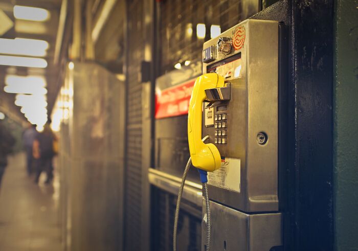 Yellow payphone mounted on a wall in a busy hallway, symbolizing calls to famous folks from history.