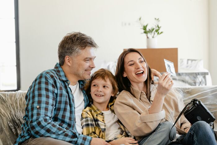 Family of three smiling together at home, enjoying a moment while looking at a photograph of historical figures.