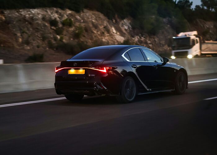 Black Lexus sedan driving on a highway at dusk with blurred background, illustrating historic figures in a modern setting.