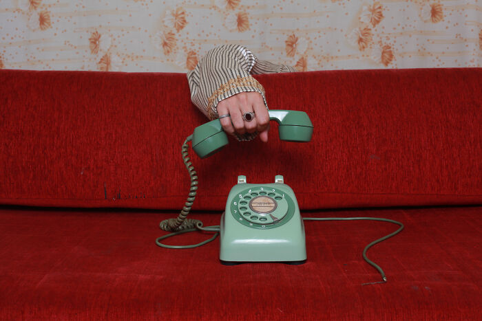 Hand holding a vintage rotary phone receiver on a red sofa, representing historical figures people would love to call.