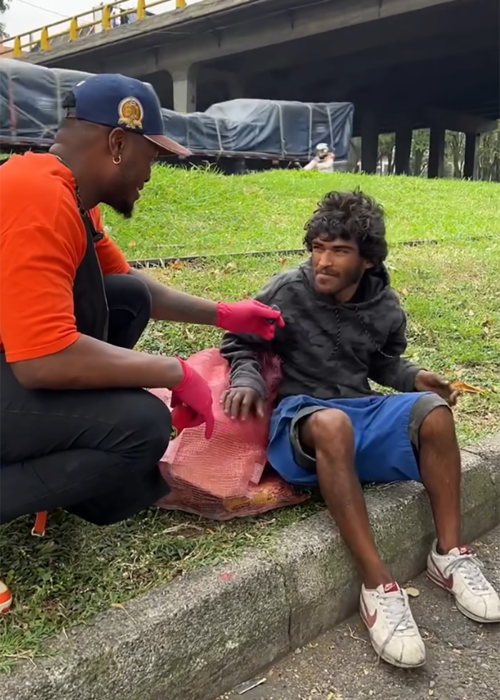 Barber wearing gloves talks with homeless man outdoors before viral makeover sparks controversy over potential model downgrade.