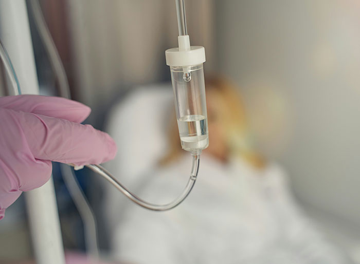 Hospital IV drip held by gloved hand with blurred patient in background, highlighting man trapped in hospital story.