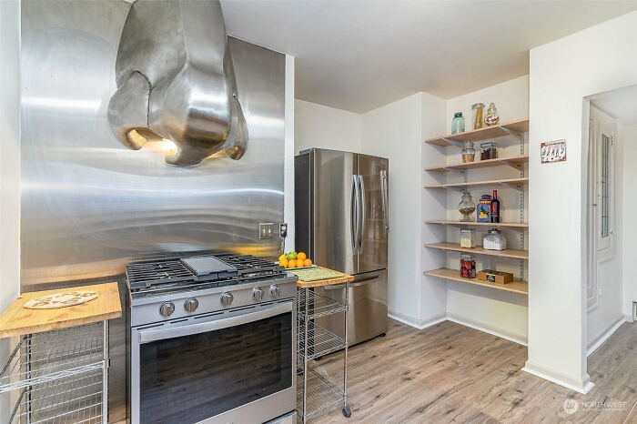 Modern kitchen with stainless steel appliances and a peculiar hand-shaped range hood featured in unhinged real estate listings.