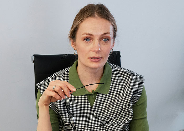 Pregnant woman holding glasses, looking concerned while discussing maternity leave eligibility with a company representative.