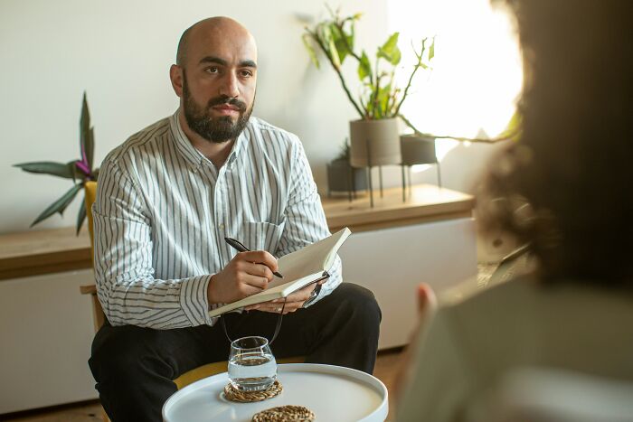 Therapist attentively listening and taking notes during a counseling session in a cozy, light-filled office setting.
