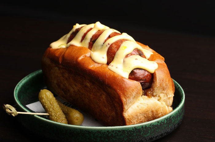 Close-up of a hot dog with mustard on a bun served with pickles, highlighting concerns about human DNA in hot dogs.