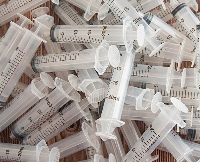 Multiple empty plastic syringes scattered on a surface, related to violence against women incidents at a music festival.