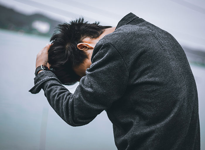 Man in dark coat holding his head by the water, reflecting on being a perfect kidney match due to close relation with his wife. Man in dark coat holding his head by the water, reflecting on being a perfect kidney match due to close relation with his wife.