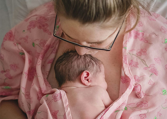 Mother in pink floral robe holding and bonding with newborn baby resting on her chest after cesarean birth.