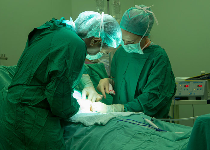 Surgeons performing a cesarean section in an operating room with medical equipment and bright surgical lights.