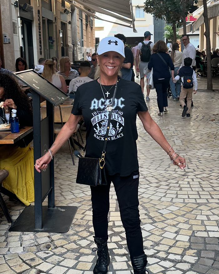 Sizzling pop star at 59 wearing a casual outfit and cap, smiling confidently on a busy street with cafes.