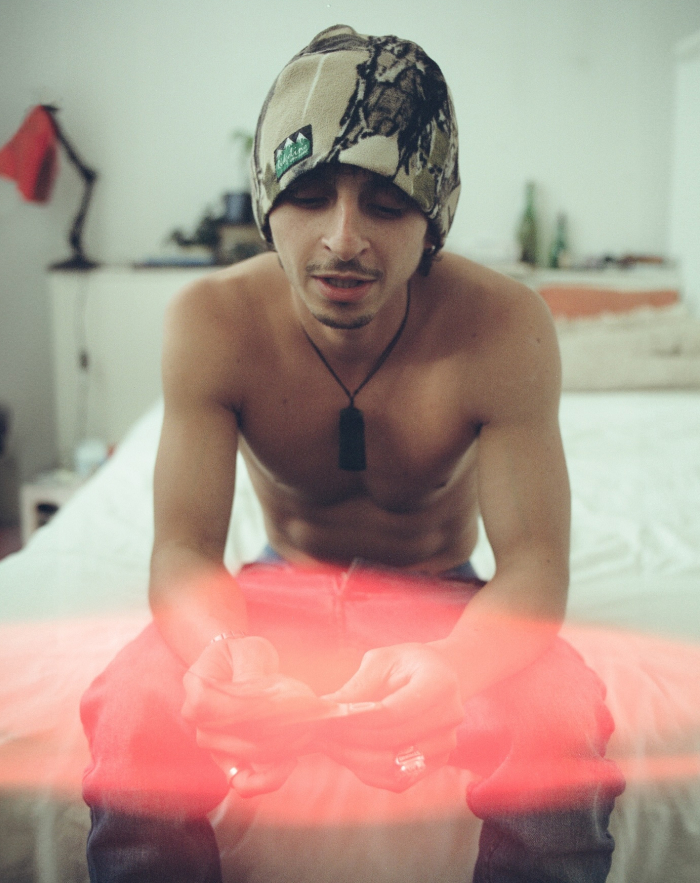 Shirtless young man wearing a patterned beanie sitting on a bed, representing a beloved character from Hannah Montana.
