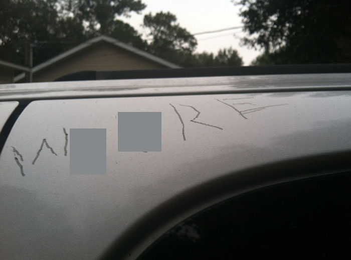 Scratched silver car door with name carved into the paint, showing damage from borrowed item misuse.