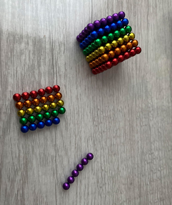 Rainbow-colored magnetic balls partially assembled with some separated on a light wooden surface showing damage from borrowing.