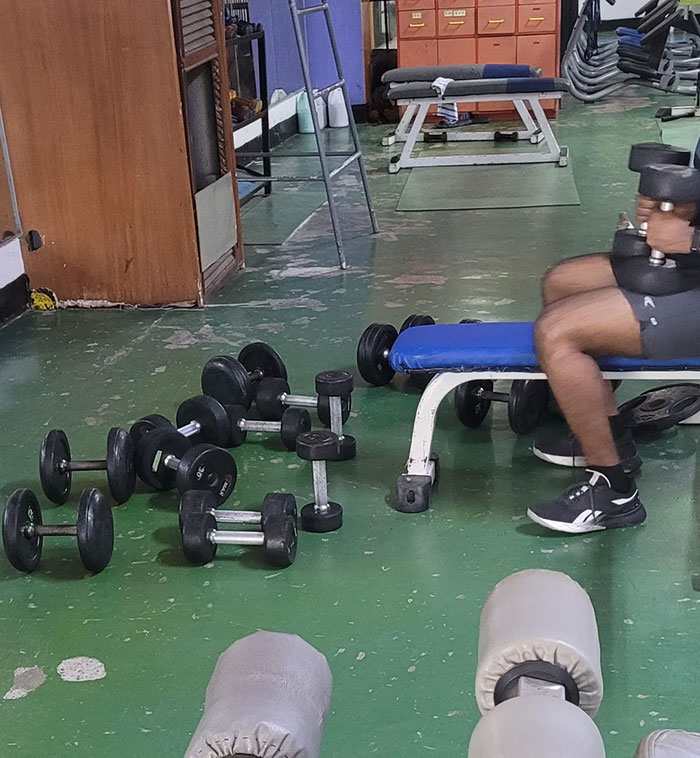 Person lifting dumbbells on a bench in a gym with scattered weights highlighting common gym moments.