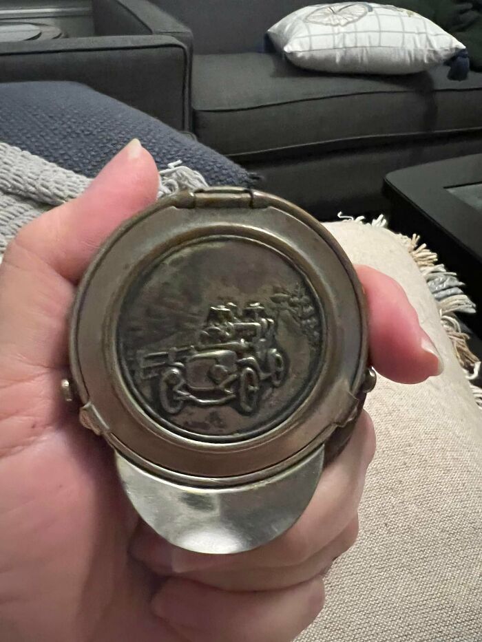 Hand holding a vintage compact with an embossed old car design, an unexpected thing found in hidden places in homes.