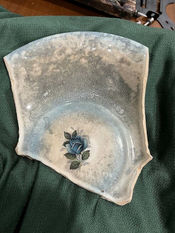 Faded broken ceramic plate with blue rose design, one of the unexpected things found in walls and hidden places in homes.