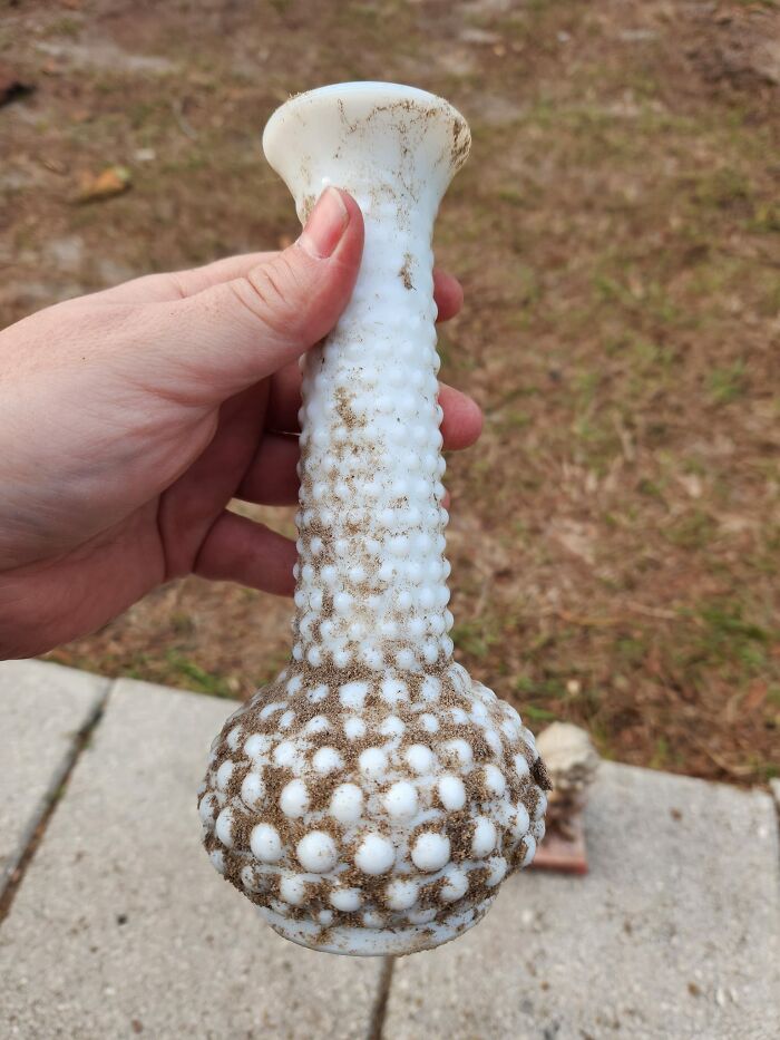 Hand holding a dirty hobnail glass vase found in walls and other hidden places in people’s homes.