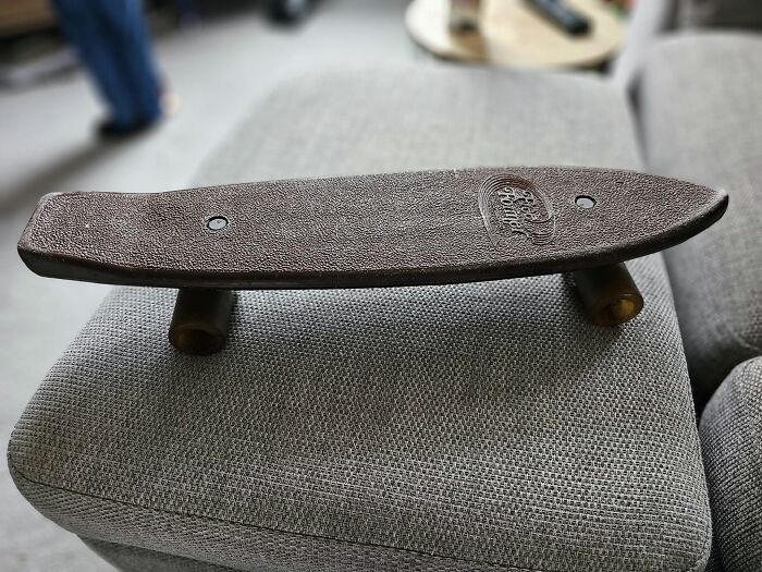 Old small skateboard hidden on gray fabric sofa, an unexpected thing found in walls and other hidden places in homes.