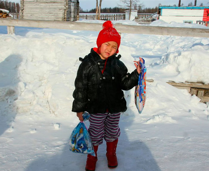Child wearing a red hat and black jacket outside in snow, holding colorful bags to keep the brain active and healthy.