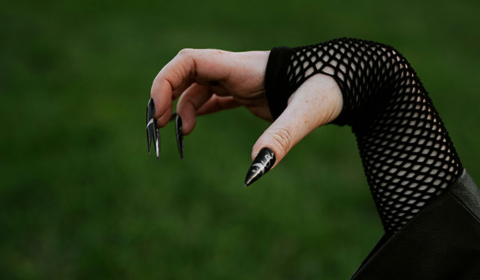 Hand with long black painted nails and fishnet sleeve against blurred green background for brain health facts.