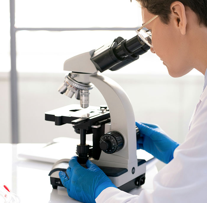 Scientist wearing blue gloves examining samples under a microscope to keep the brain active and healthy.