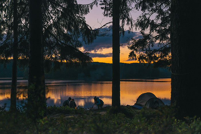 Campers by a lakeside at sunset, surrounded by trees, illustrating nature's role in keeping the brain active and healthy