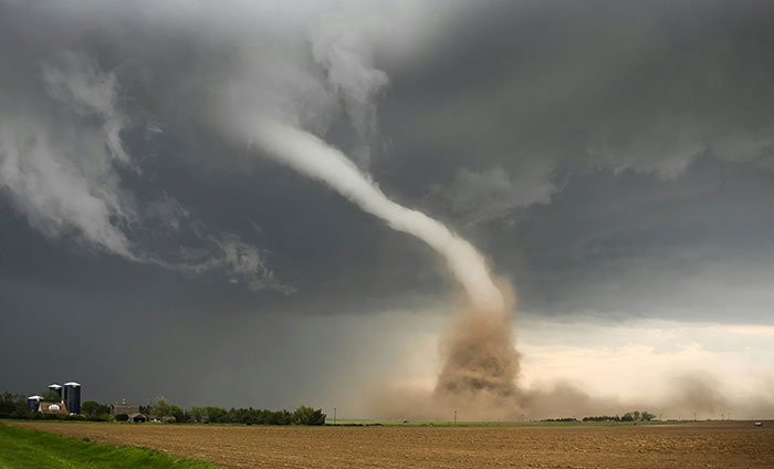 A large tornado touching down in a flat rural field under dark storm clouds, illustrating powerful natural forces.