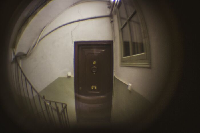 View through a peephole showing a dark wooden door in a narrow stairwell, illustrating uncommon hacks for women living alone.