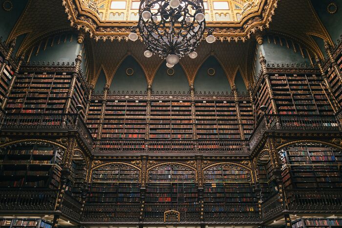 Ornate historic library interior with floor-to-ceiling shelves filled with books and a large decorative chandelier above.