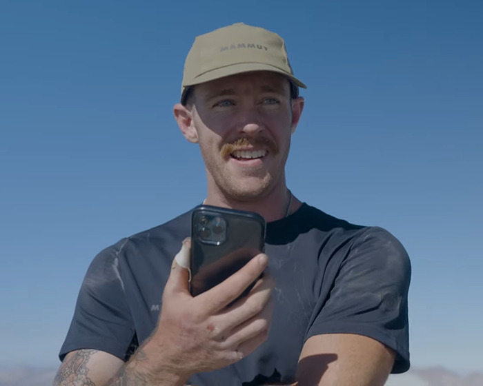 Man wearing beige cap and black shirt holding phone outdoors discussing Jiu-Jitsu trainer and beginner student injury settlement.