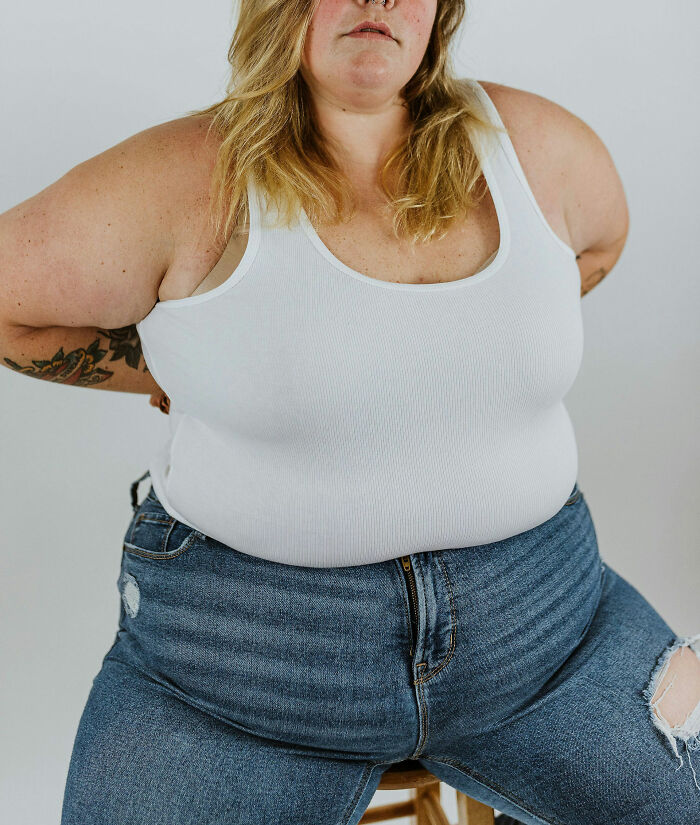 Person wearing a white tank top and blue jeans sitting, related to insane hospital experiences in a medical drama context.