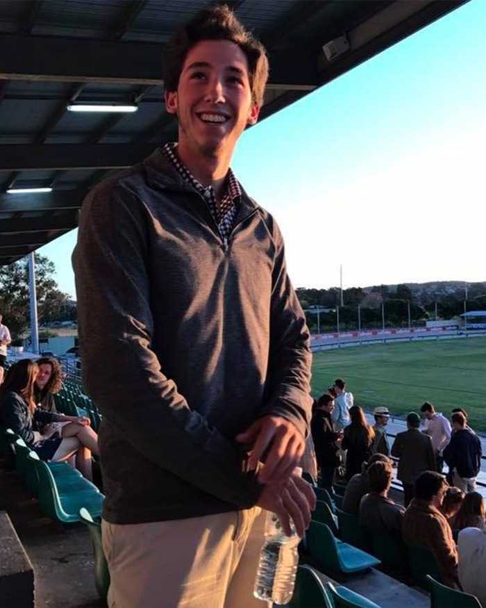 Young man smiling and holding a water bottle at a sports stadium, related to honeymoon tragedy in ankle-deep water.