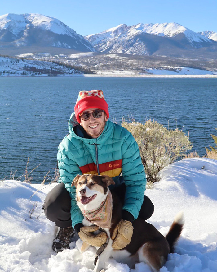 Man wearing winter clothing with dog by snowy lakeside, reflecting a newlywed&rsquo;s honeymoon tragedy near ankle-deep water.