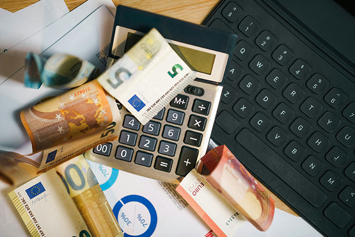 Calculator with euro banknotes on financial documents next to a keyboard, illustrating Excel document challenges. Calculator with euro banknotes on financial documents next to a keyboard, illustrating Excel document challenges.