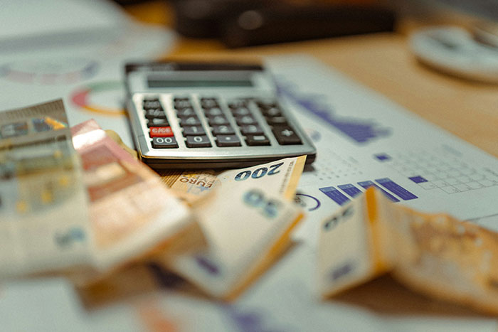 Calculator on a desk with scattered Euro banknotes and charts, illustrating frustration over reading an Excel document. Calculator on a desk with scattered Euro banknotes and charts, illustrating frustration over reading an Excel document.