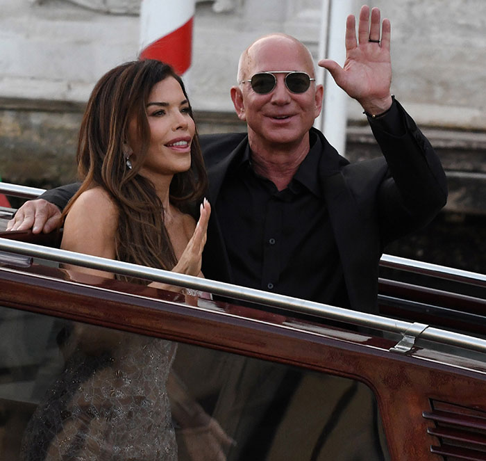 Jeff Bezos and Lauren S&aacute;nchez waving on a boat during their wedding event attended by high-profile guests.