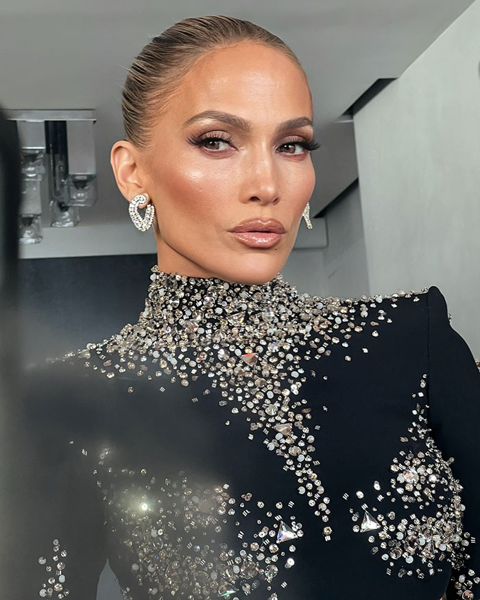 Jennifer Lopez posing in a black outfit adorned with sparkling crystals, facing camera with a neutral expression indoors.