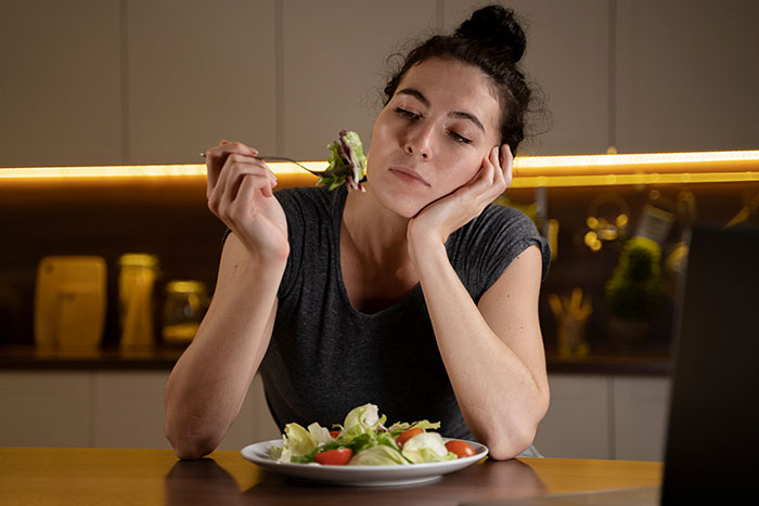 Young woman looking reluctant eating salad, highlighting challenges of bacon in meals with Jewish dietary preferences.