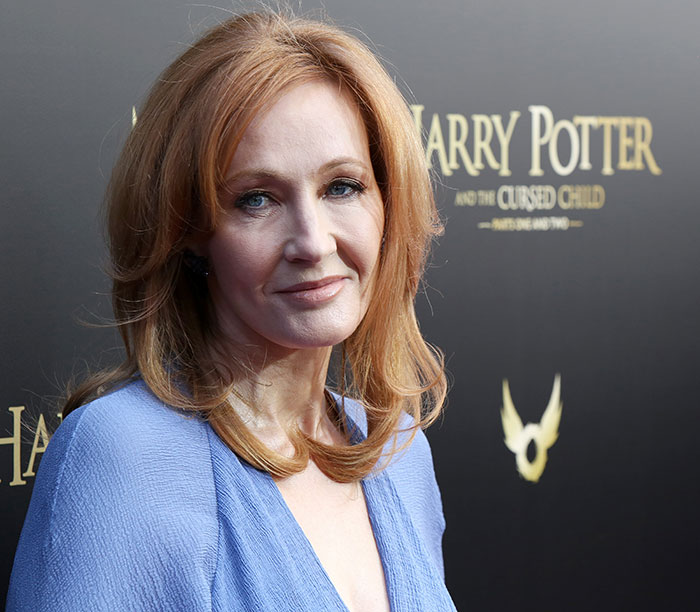 J.K. Rowling smiling on the Harry Potter and the Cursed Child red carpet event with fans in attendance.